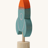 A side view of a Grimms blue wooden decorative figure with a red nose showing the thickness of the figure