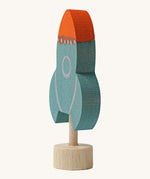 A side view of a Grimms blue wooden decorative figure with a red nose showing the thickness of the figure