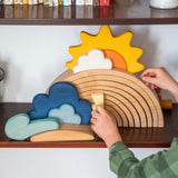 A close up of a child placing pieces from the Grimm's weather set on a 12 piece rainbow that's on a shelf.