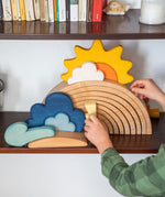 A close up of a child placing pieces from the Grimm's weather set on a 12 piece rainbow that's on a shelf.