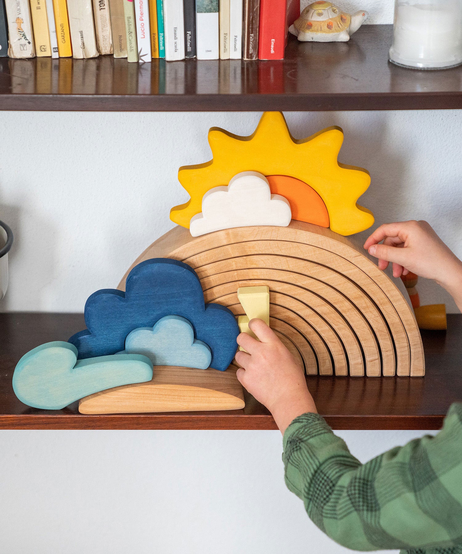 A close up of a child placing pieces from the Grimm's weather set on a 12 piece rainbow that's on a shelf.