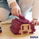 Close up of child's hand placing a Kapla eco-friendly wooden block on top of a wooden stack