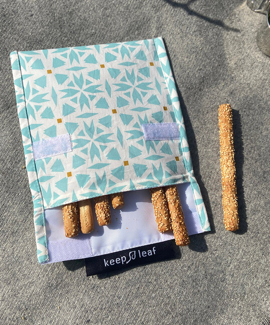A close up of the organic cotton geo Keep Leaf large baggie outside on a blanket opened with food inside