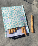 A close up of the organic cotton geo Keep Leaf large baggie outside on a blanket opened with food inside