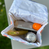 A opened Keep Leaf insulated lunchbag on a table showing food packed inside. Features a pouch for a name tag on the inside of the lid