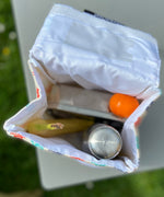 A opened Keep Leaf insulated lunchbag on a table showing food packed inside. Features a pouch for a name tag on the inside of the lid