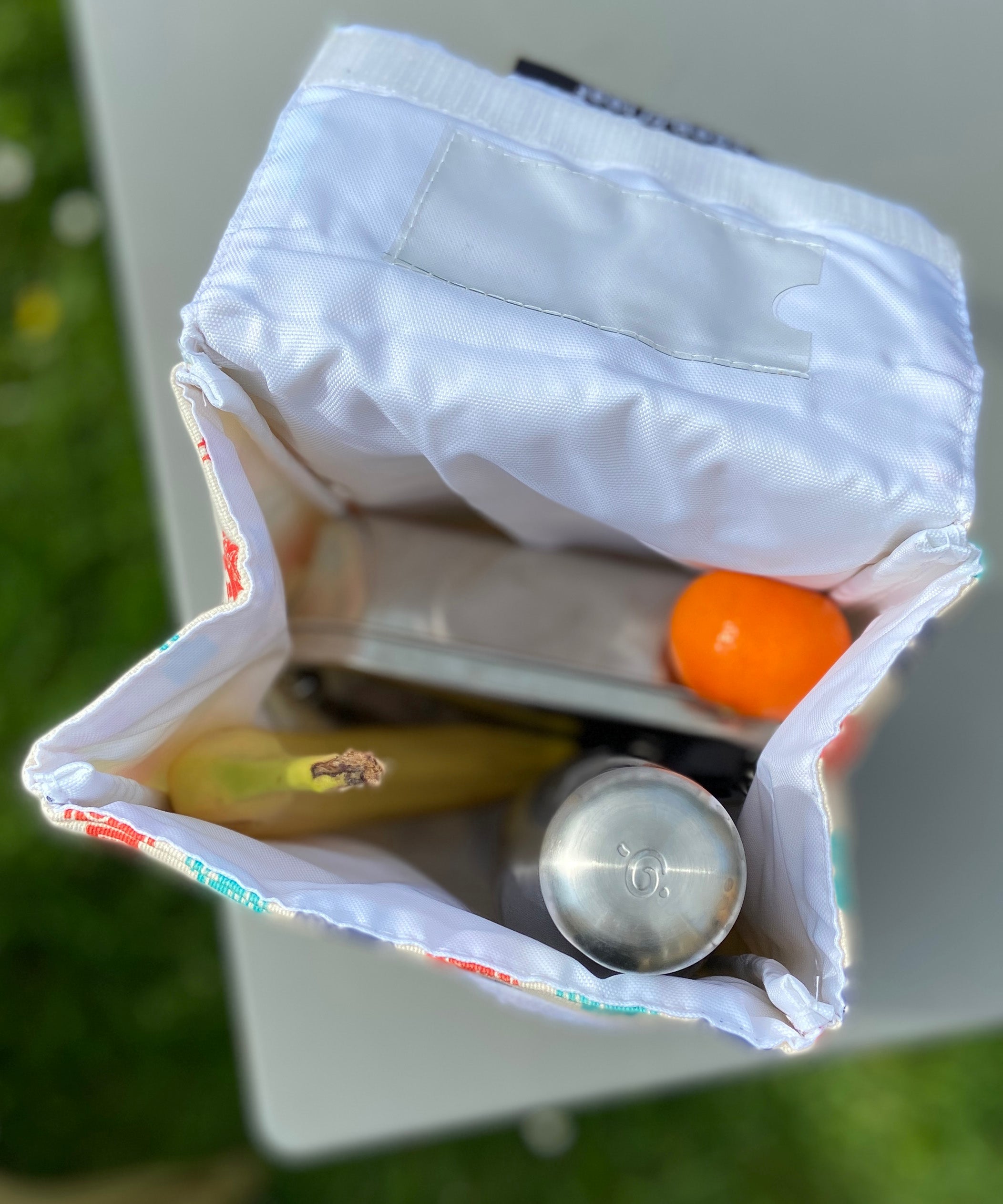 A opened Keep Leaf insulated lunchbag on a table showing food packed inside. Features a pouch for a name tag on the inside of the lid