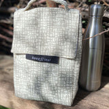 Keep Leaf insulated lunchbag in mesh design outside on a wooden surface next to a drinking bottle for size reference.