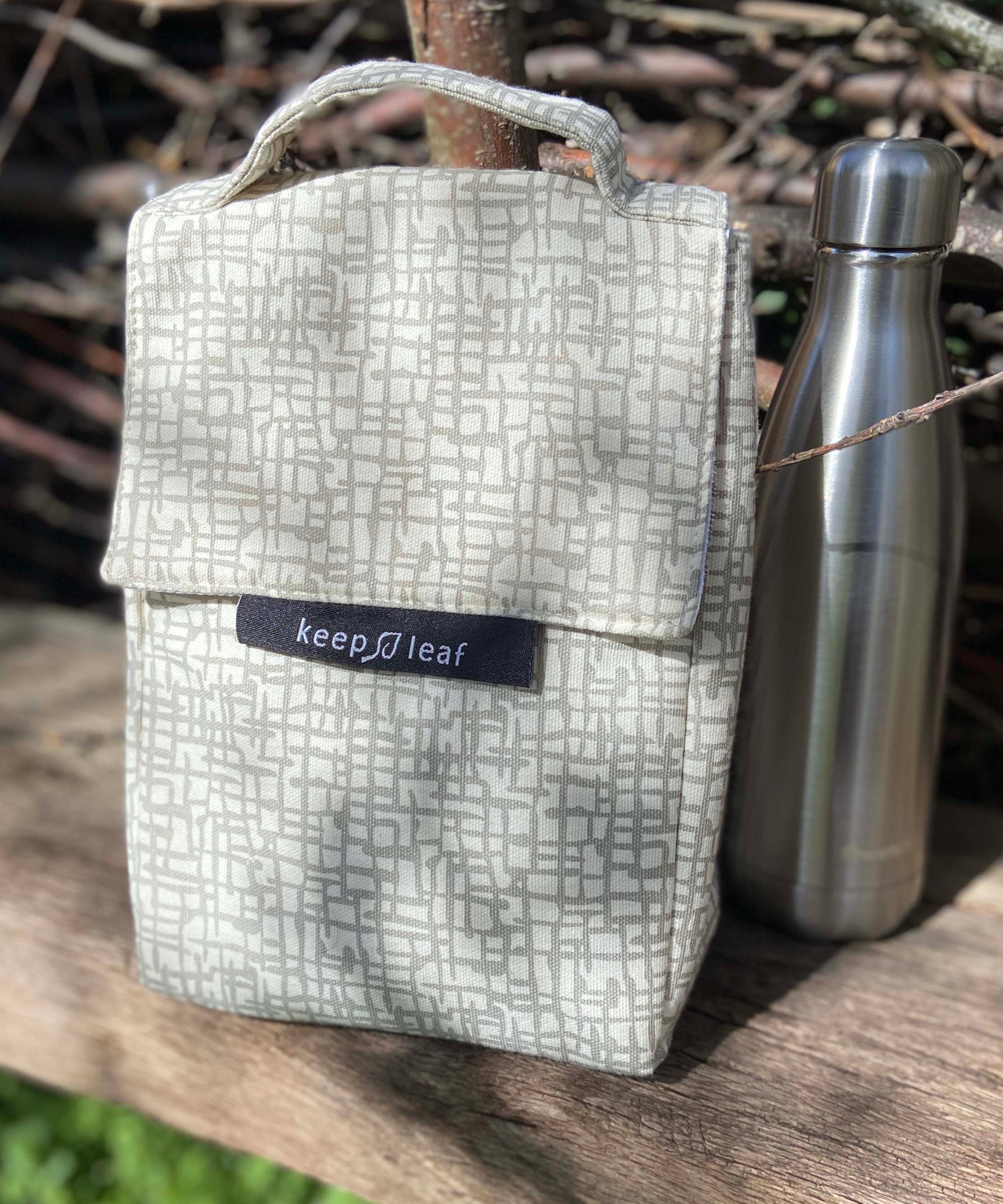 Keep Leaf insulated lunchbag in mesh design outside on a wooden surface next to a drinking bottle for size reference.