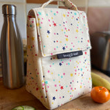 Keep Leaf insulated lunchbag in stars design in the kitchen on a wooden surface surrounded by food and a drinking bottle for size reference.