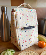 Keep Leaf insulated lunchbag in stars design in the kitchen on a wooden surface surrounded by food and a drinking bottle for size reference.