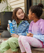 Two children sitting on a step outdoors, one child is holding a Rainbow print Kid Kanteen 12oz Insulated Flip Seal Sport Cap Bottle.