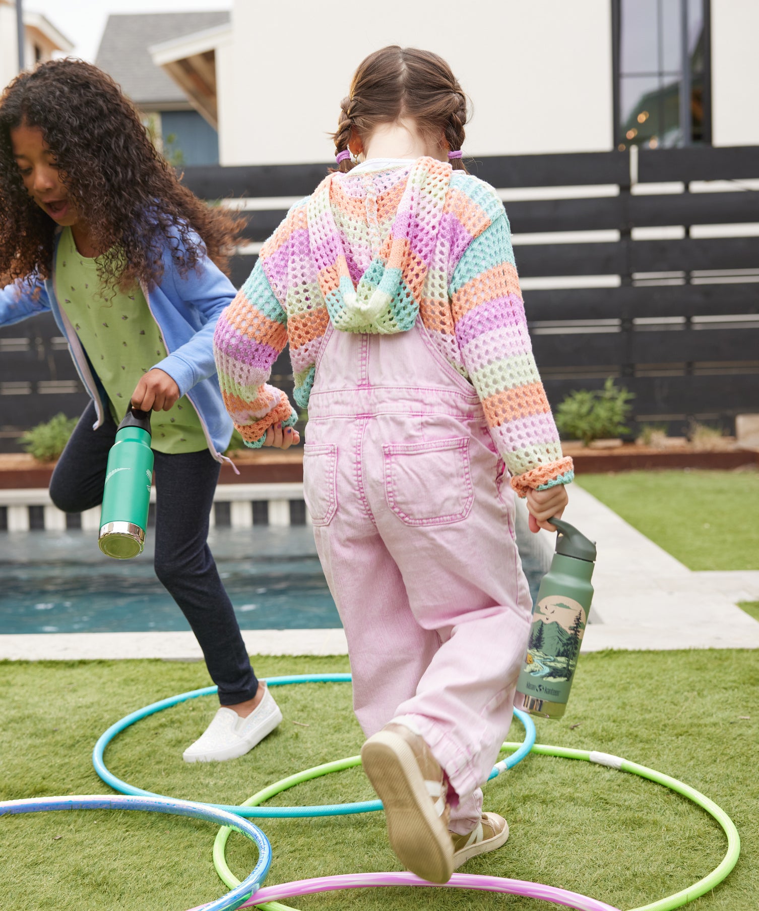 Two children playing outdoors, one has a Mountain Scape Kid Kanteen 12oz Insulated Flip Seal Sport Cap Bottle and the other has a Dino Skate print bottle.