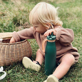 An adult looking up whilst standing still in front of a white brick building with a metal fence. The adult is wearing a purple back pack carrying the One Green Bottle 500ml Evolution Collection Bottle - Sports Cap in a side pocket on the outside of the ba