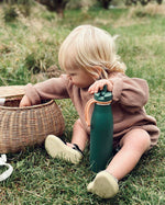 An adult looking up whilst standing still in front of a white brick building with a metal fence. The adult is wearing a purple back pack carrying the One Green Bottle 500ml Evolution Collection Bottle - Sports Cap in a side pocket on the outside of the ba