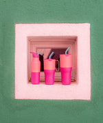 Klean Kanteen 16oz, 26 oz and 36oz rise insulated stainless steel bottle and tumblers standing in front of a window surrounded by white and green wall showing the pink colour way and handle detail on the tumblers