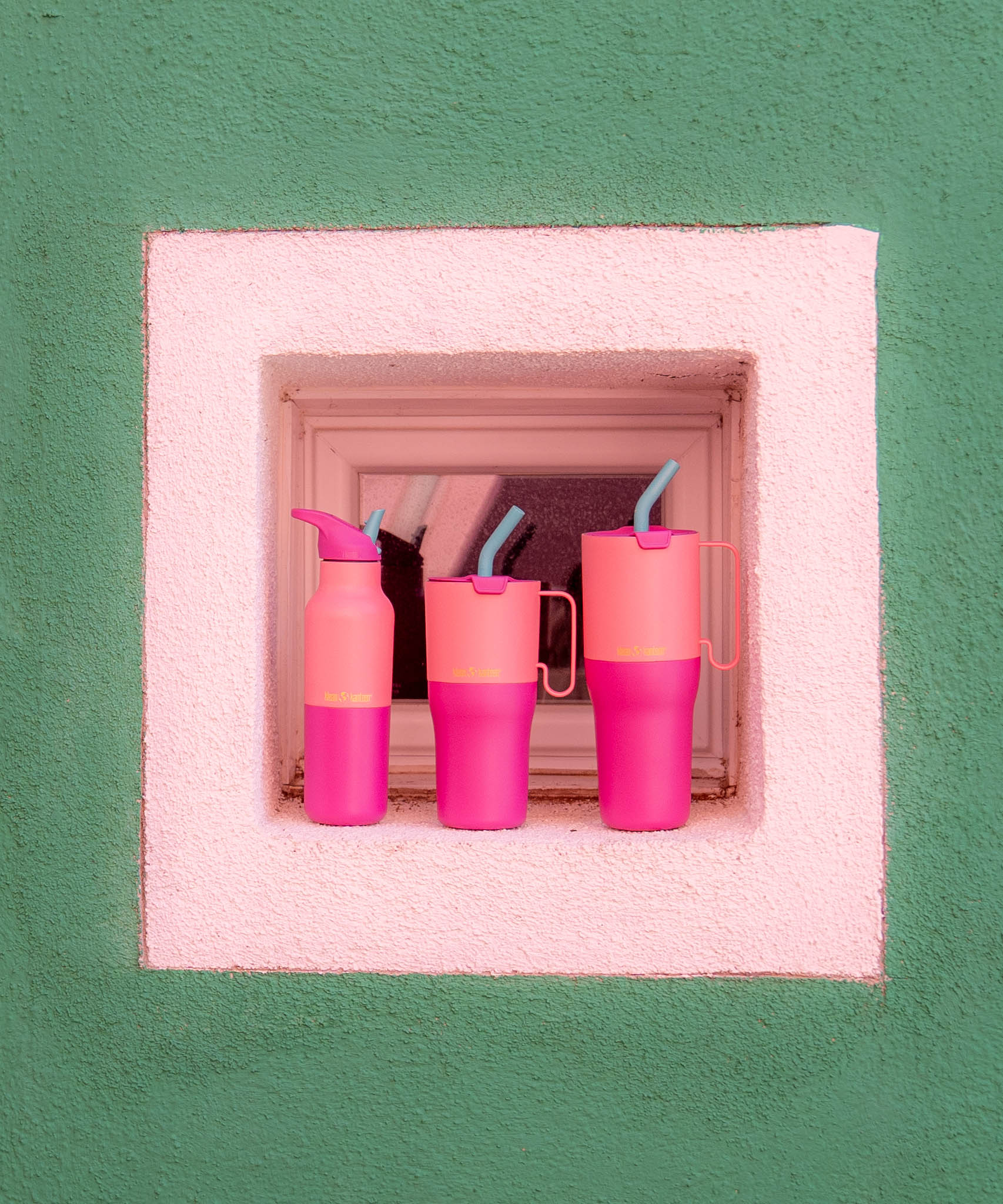 Klean Kanteen 16oz, 26 oz and 36oz rise insulated stainless steel bottle and tumblers standing in front of a window surrounded by white and green wall showing the pink colour way and handle detail on the tumblers