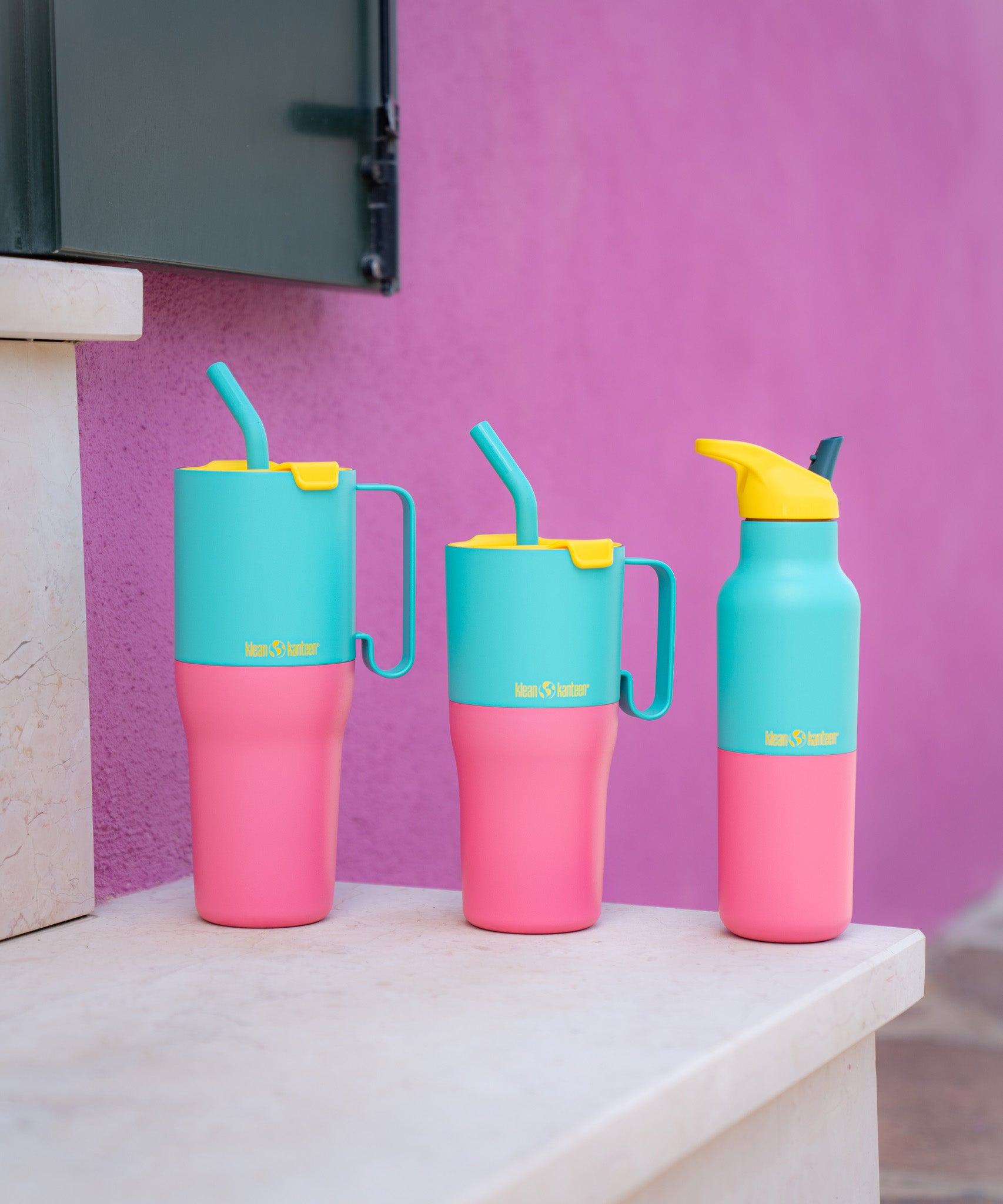 Klean Kanteen turquoise kaleidoscope 16oz, 26oz and 36oz rise insulated stainless steel bottle and tumblers on a stone surface and a purple wall showing the scale and the vibrant pink and turquoise colour way design and handle detail on the tumblers