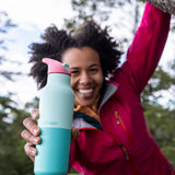 A woman hanging from a tree outside and holding the bay 16oz stainless steel reusable klean kanteen insulated rise bottle