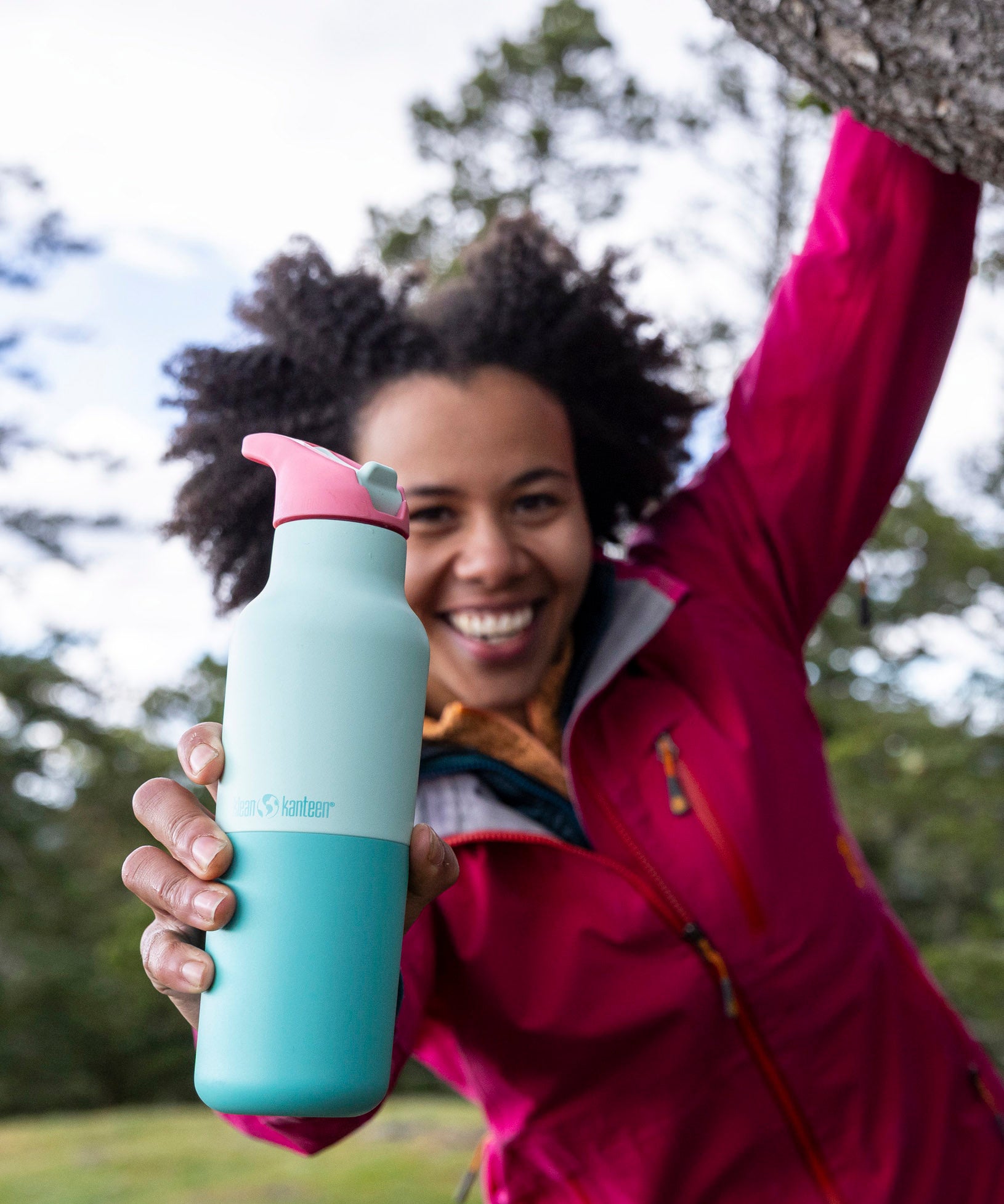 A woman hanging from a tree outside and holding the bay 16oz stainless steel reusable klean kanteen insulated rise bottle