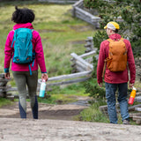 A woman and man walking outside on a gravel road and holding the bay and marigold 16oz stainless steel reusable klean kanteen insulated rise bottles