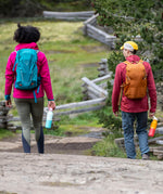 A woman and man walking outside on a gravel road and holding the bay and marigold 16oz stainless steel reusable klean kanteen insulated rise bottles