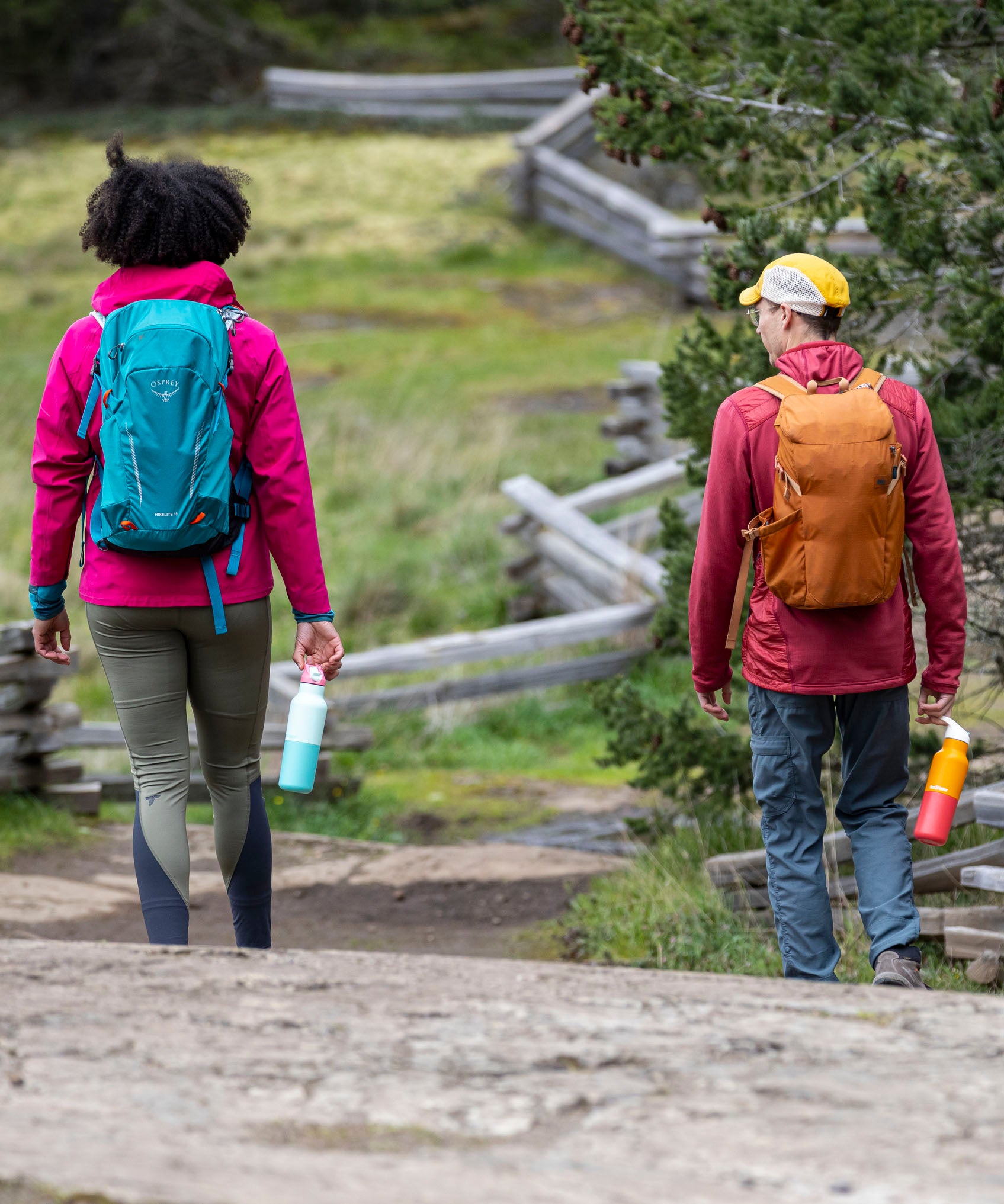 A woman and man walking outside on a gravel road and holding the bay and marigold 16oz stainless steel reusable klean kanteen insulated rise bottles