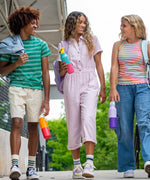 3 young adults walking outside and holding the marigold, turquoise and orchid 16oz stainless steel reusable klean kanteen insulated rise bottles showing scale of each bottle