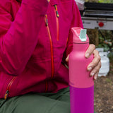 A close up of a adult hand holding the pink lemonade Klean Kanteen 16 oz rise insulated rise bottle showing the colour way  design and matching flip sports cap detail.