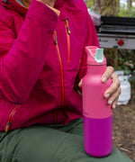 A close up of a adult hand holding the pink lemonade Klean Kanteen 16 oz rise insulated rise bottle showing the colour way  design and matching flip sports cap detail.