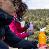 A man and a woman standing on a high bridge and holding the marigold and orchid 16oz Klean Kanteen stainless steel reusable rise insulated bottles