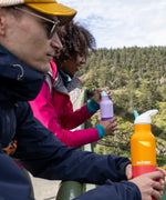 A man and a woman standing on a high bridge and holding the marigold and orchid 16oz Klean Kanteen stainless steel reusable rise insulated bottles