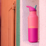 A pink lemonade 16oz Klean Kanteen stainless steel insulated rise bottle standing  on a  white wall