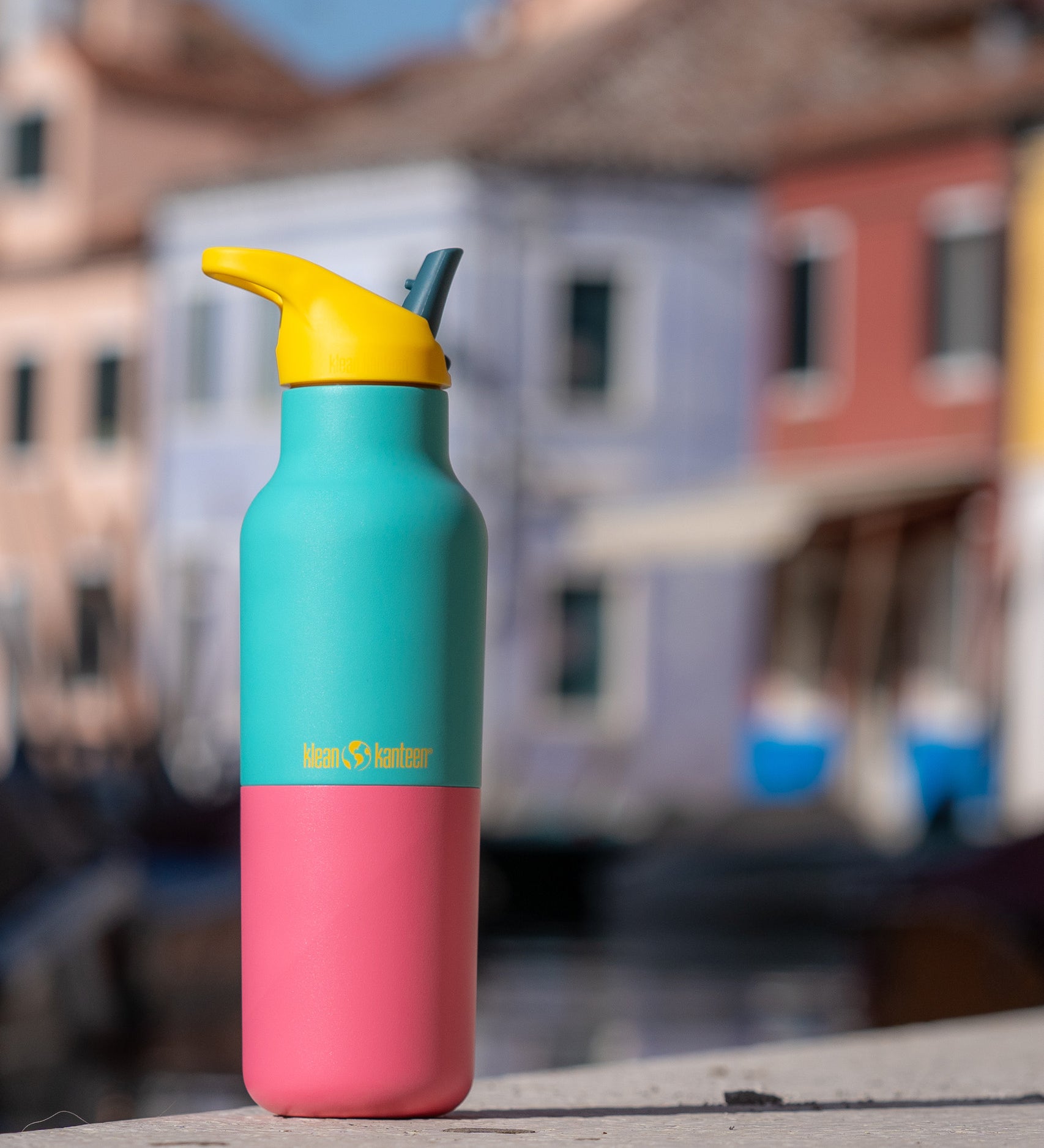 A klean Kanteen 16oz reusable stainless steel rise insulated bottle on a stone wall  showing the blue and pink kaleidoscope colour way design with the yellow flip sports lid