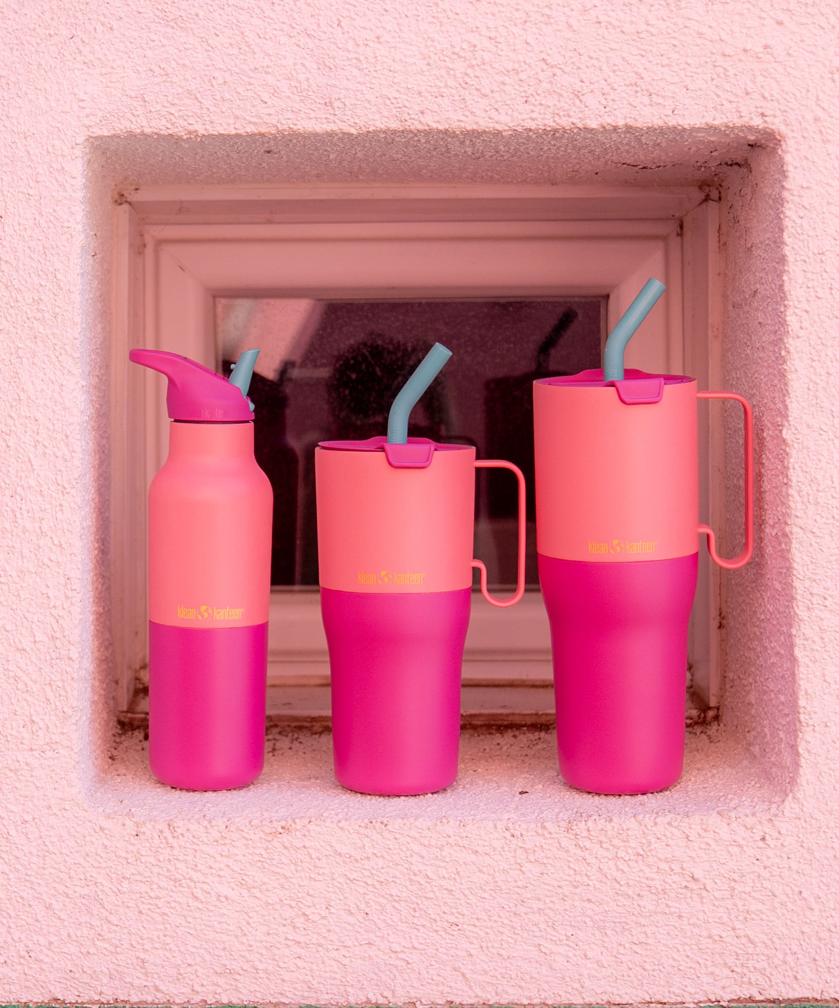 Klean Kanteen pink lemonade kaleidoscope 16oz, 26 oz and 36oz rise insulated stainless steel bottle and tumblers standing in front of a window showing the pink colour way and handle detail on the tumblers