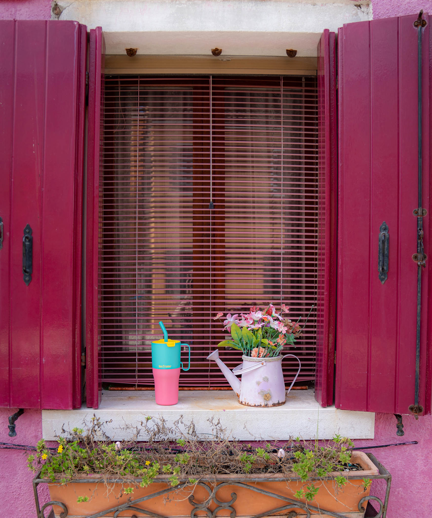 A Klean Kanteen 26oz turquoise kaleidoscope stainless steel insulated rise tumbler on a windowsill next to a watering can for scale showing the pink and turquoise colour way with a yellow flip cap. Features a turquoise handle on the side with a matching straw