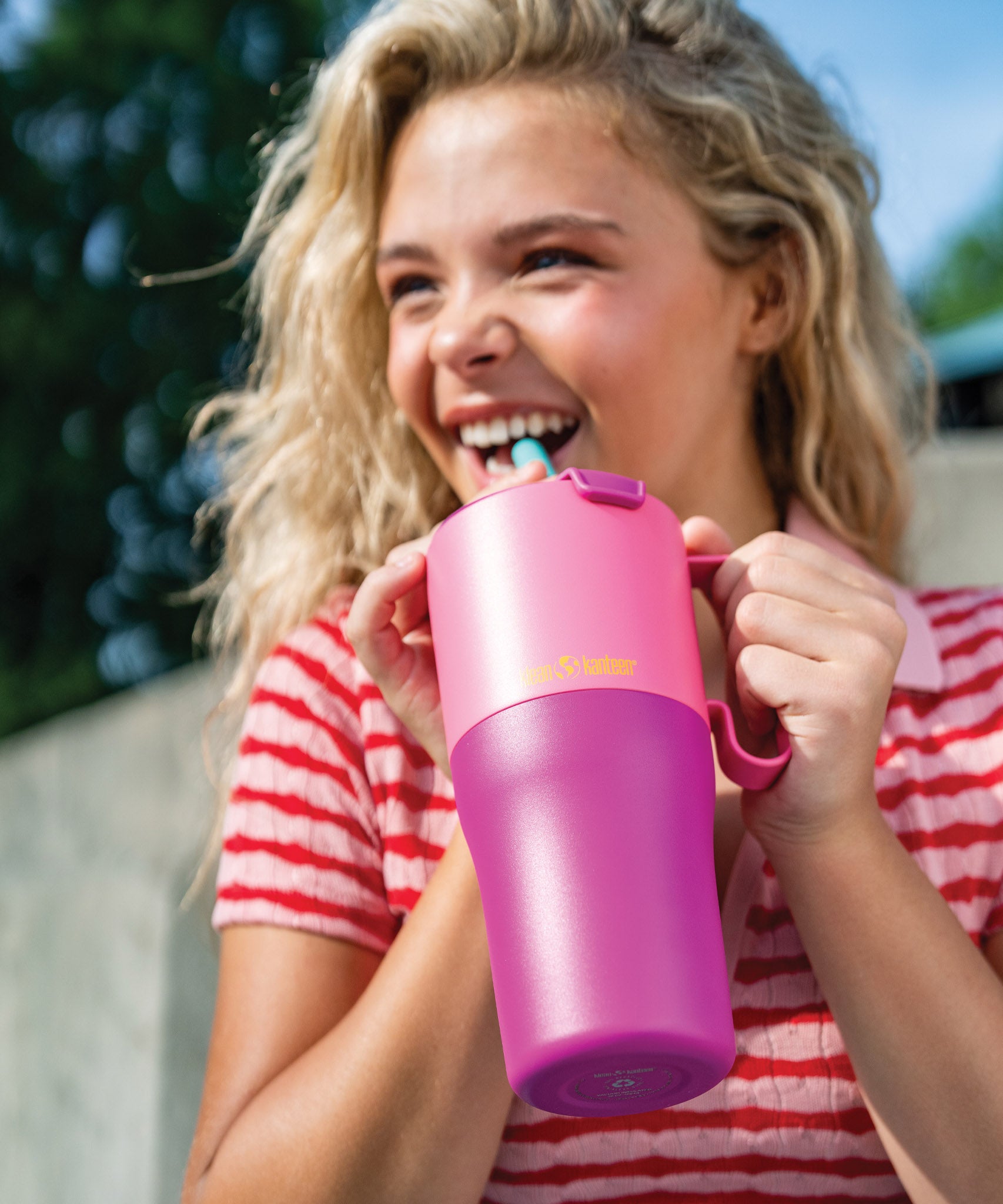 A young adult holding the 26oz pink lemonade kaleidoscope 26oz Klean Kanteen rise insulated stainless steel tumbler by the handle on the side showing the scale