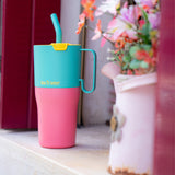 A close up of the Klean Kanteen 26oz turquoise stainless steel insulated rise tumbler on a windowsill showing the pink and turquoise colour way with a yellow flip cap. Features a turquoise handle on the side with a matching straw
