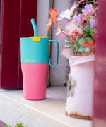 A close up of the Klean Kanteen 26oz turquoise stainless steel insulated rise tumbler on a windowsill showing the pink and turquoise colour way with a yellow flip cap. Features a turquoise handle on the side with a matching straw
