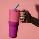 A adult hand holding the 36 pink lemonade Klean Kanteen stainless steel insulated tumbler by the pink handle on the side showing the scale of the tumbler and turquoise straw detail