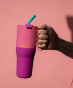 A adult hand holding the 36 pink lemonade Klean Kanteen stainless steel insulated tumbler by the pink handle on the side showing the scale of the tumbler and turquoise straw detail
