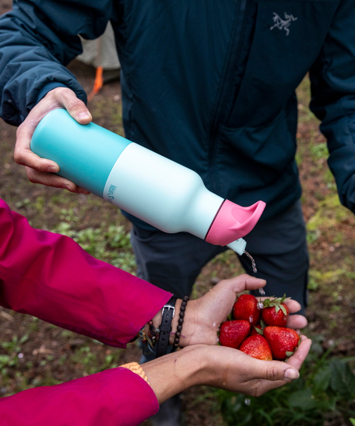 A adult holding the bay kaleidoscope 16oz Klean Kanteen insulated rise bottle by the bottom and pouring water into a handful of strawberries.