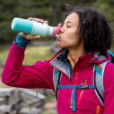 A woman standing outside and drinking from the Klean Kanteen 16oz bay kaleidoscope stainless steel reusable insulated rise bottle