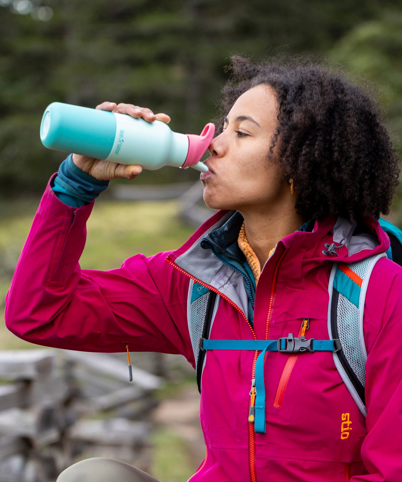 A woman standing outside and drinking from the Klean Kanteen 16oz bay kaleidoscope stainless steel reusable insulated rise bottle