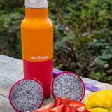 A close up of the marigold kaleidoscope 16oz Klean Kanteen reusable stainless steel rise bottle showing the orange and red colourway with white sports cap detail  on top of a wooden surface next to a bunch of fruit