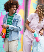 2 young adults holding the marigold and turquoise kaleidoscope 16oz Klean Kanteen insualted rise bottles by their flip sports cap showing scale and colour way designs