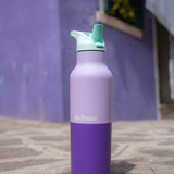 A close up of the orchid kaleidoscope 16oz klean kanteen insulated stainless steel rise bottle on a stone path showing the purple colour way with turquoise flilp sports cap detail