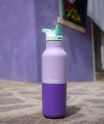 A close up of the orchid kaleidoscope 16oz klean kanteen insulated stainless steel rise bottle on a stone path showing the purple colour way with turquoise flilp sports cap detail