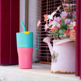 A close up of the turquoise kaleidoscope Klean Kanteen 26oz rise insulated tumbler on a windowsill  next to a watering can showing the pink and turquoise colour way design with the turquoise straw and handle detail