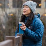 A person looking into the distance whilst holding a Klean Kanteen 12oz TKWide Cafe in the corsair colour on a wooden fence.